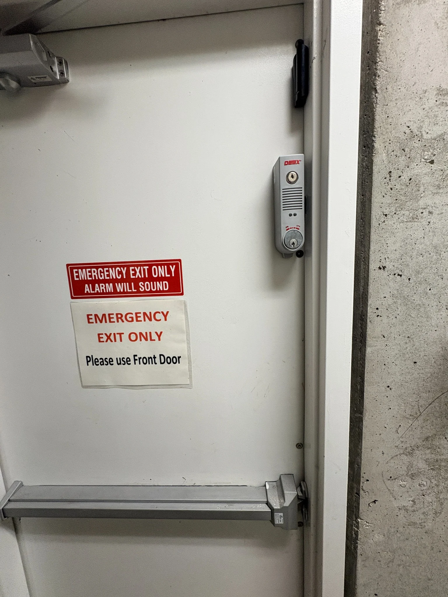 Detex door-prop alarm and black Ajax door contact on a Calladine parkade exit door with a push bar in Vancouver